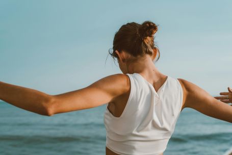 Back view of a woman in athletic attire enjoying a serene moment by the ocean.